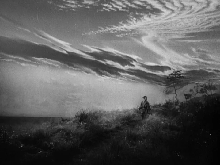 The Men Who Tread on the Tigers Tail (1945) movie still: wide — A grassy coastal hillside under a dramatic, expansive sky filled with wispy clouds.…