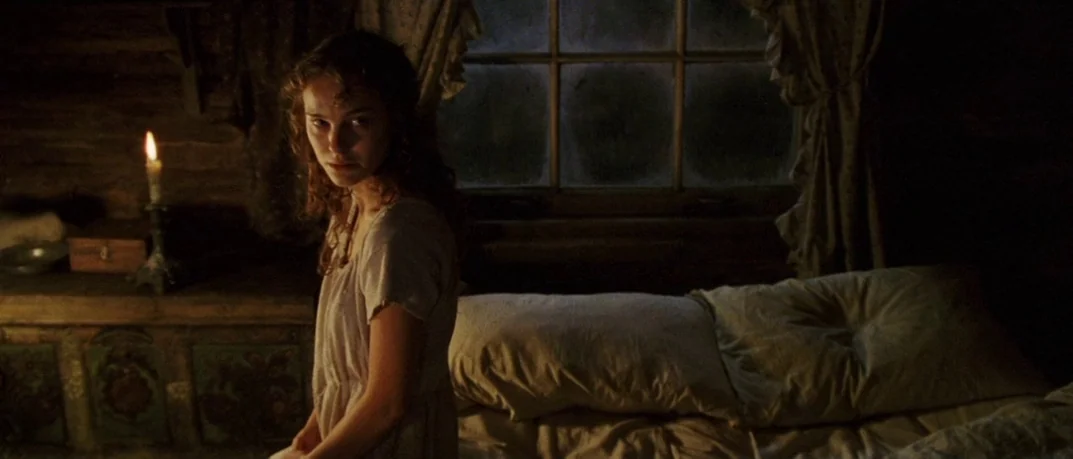 Cold Mountain (2003) movie still: medium — A dark wooden room contains a bed with rumpled linens and a small candle. A young woman in a simple…