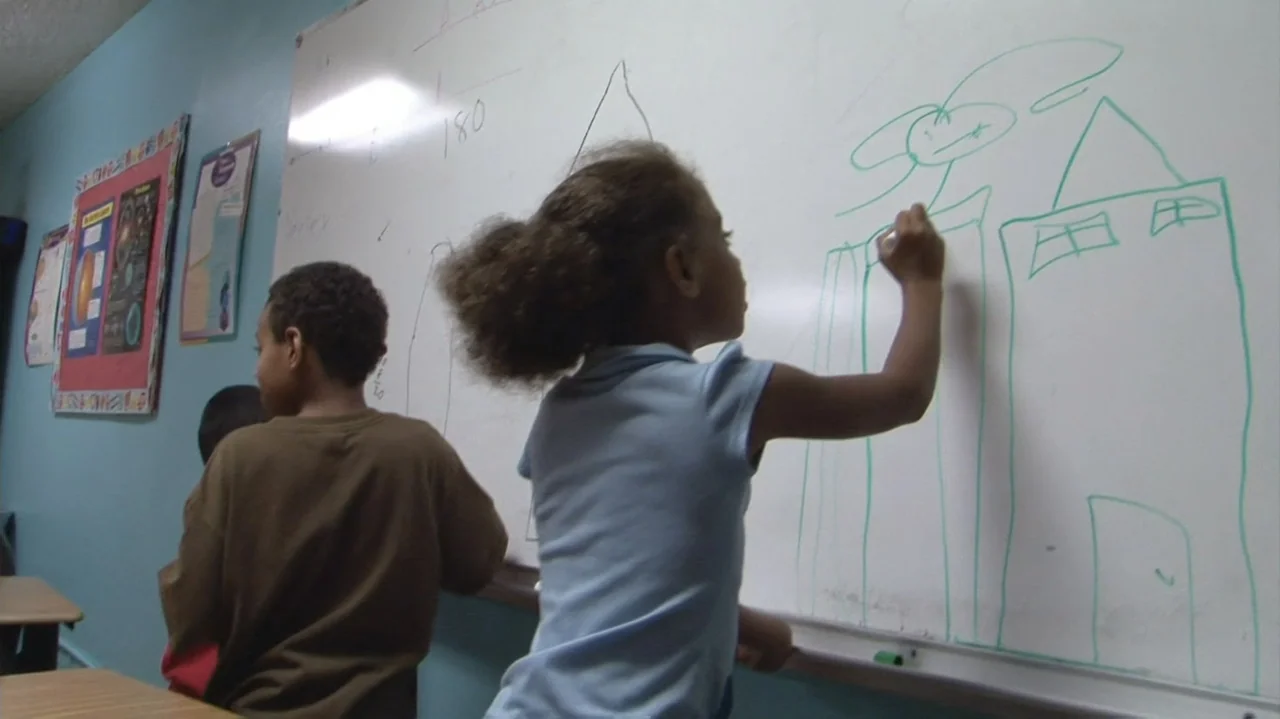 Homeless: The Motel Kids of Orange County (2010) movie still: medium — A light-walled classroom features a large white marker board covered in green…