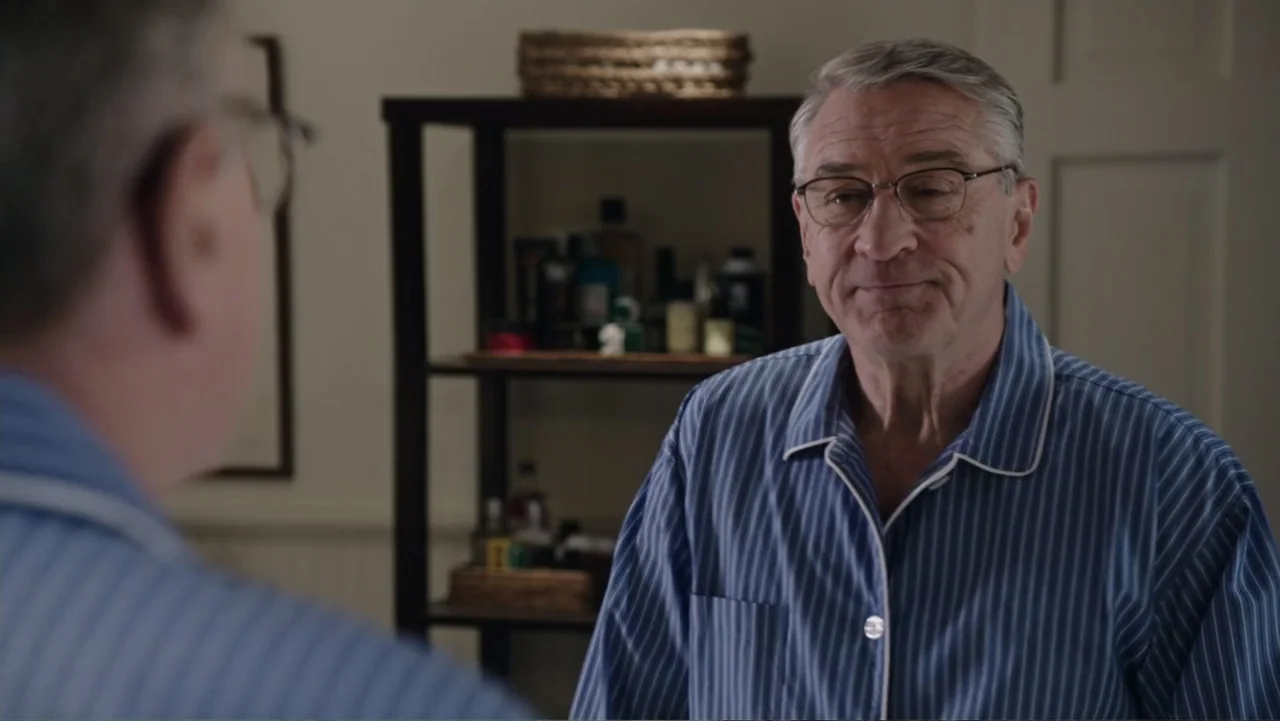 The Intern (2015) movie still: medium — A residential bathroom interior features a dark shelving unit against a plain wall. An older man wearing…