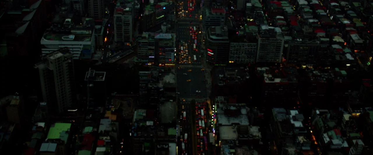 Lucy (2014) movie still: establishing — An aerial view of a dense urban grid at night with illuminated avenues. Numerous buildings of varying…