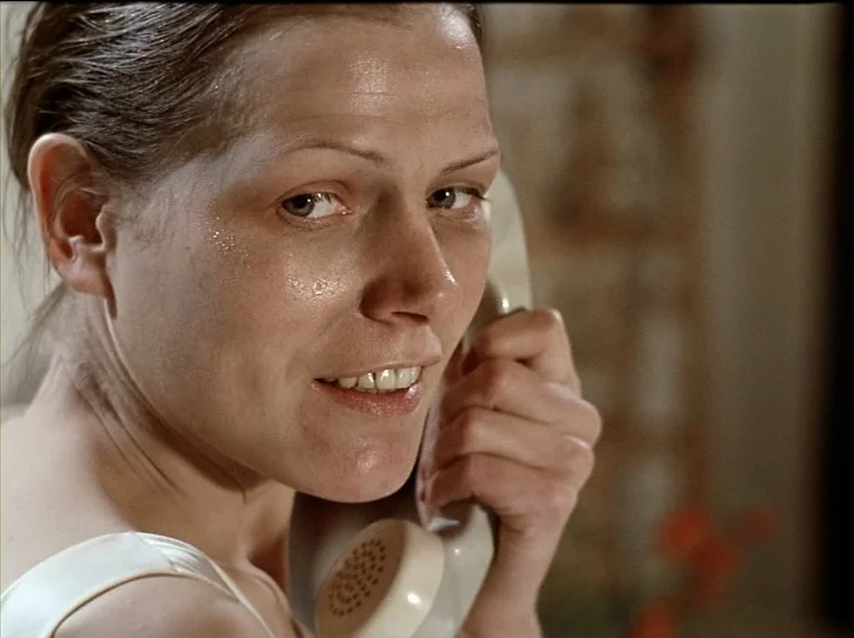 The Bitter Tears Of Petra Von Kant (1972) movie still: closeup — A woman stands indoors against a light-colored wall with a blurred background. She…