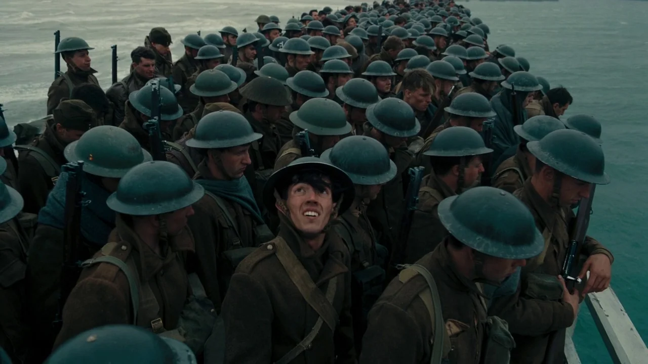 Dunkirk (2017) movie still: wide — A crowded deck of a ship is packed with dozens of soldiers in military attire. The men stand shoulder to shoulder…