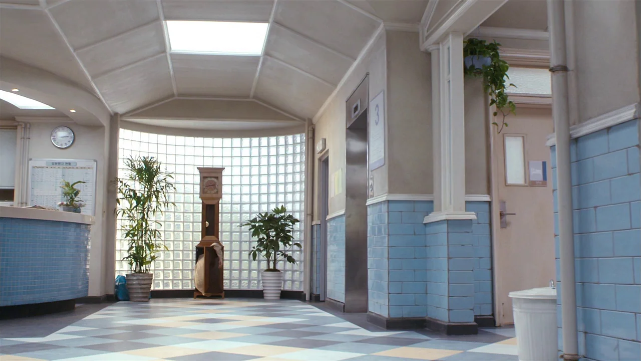 I’m A Cyborg, But That’s Okay (2006) movie still: wide — A hospital hallway features light blue tiled wainscoting and a glass block rear wall. An…