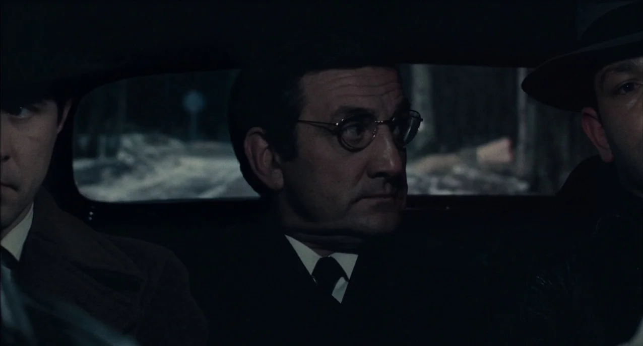 The Army of Shadows (1969) movie still: medium — Three men sit together in the dim cabin of a car during the night. The vehicle moves along a dark…