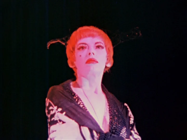 Inauguration of the Pleasure Dome (1954) movie still: medium — A figure stands on a dark stage with a black background. The person wears decorative…