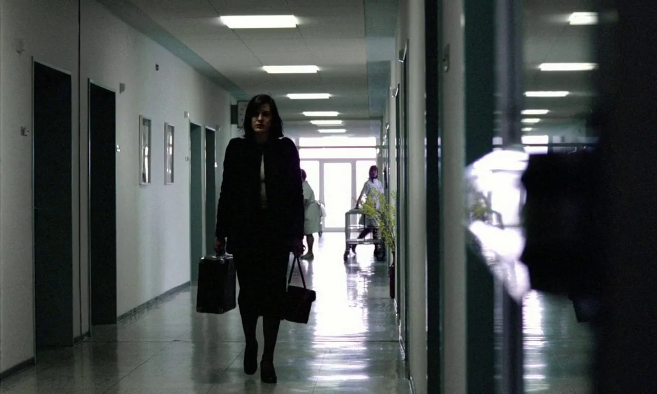 The Lost Honour of Katharina Blum (1975) movie still: fullbody — A long, clinical hospital hallway with white walls and tiled floors stretches into…