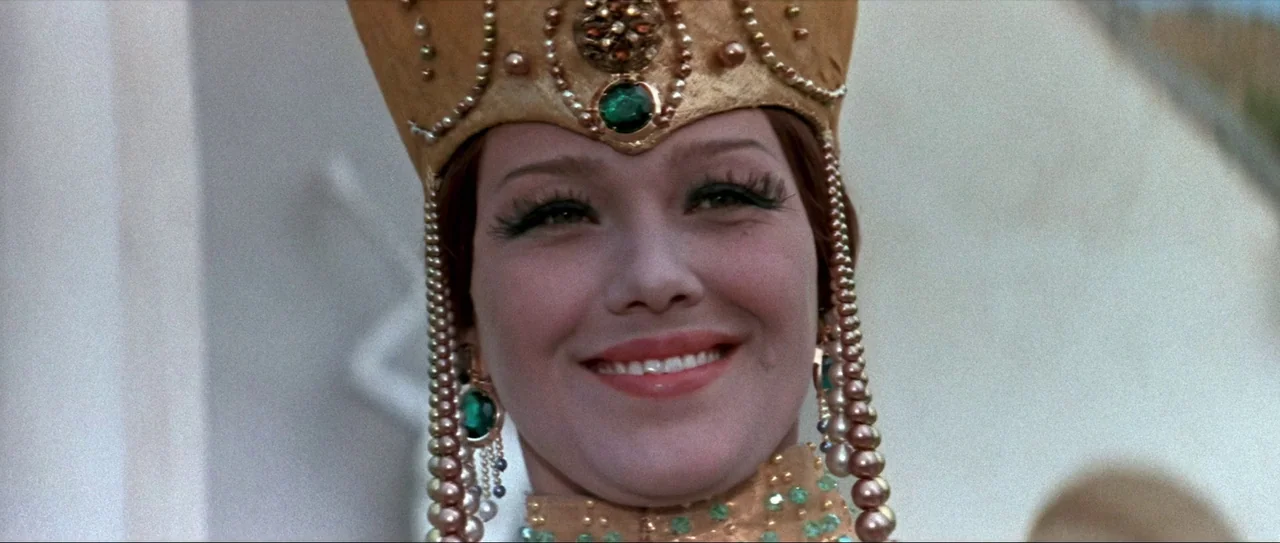 Through Fire, Water and… Brass Pipes (1968) movie still: closeup — A woman wears an elaborate, jewel-encrusted golden headdress during an outdoor…