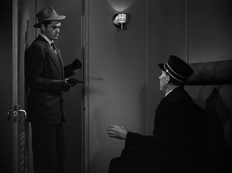 White Heat (1949) movie still: medium — A train compartment with a simple wall sconce and a padded seat. A man in a hat points a gun at a conductor…