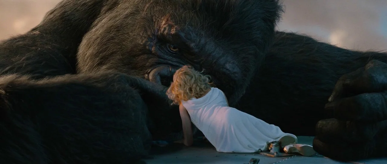 King Kong (2005) movie still: medium — A gargantuan gorilla lies on a metallic surface atop a building at night. A woman in a white dress kneels…