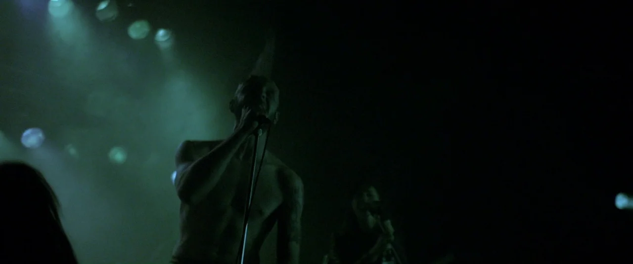 The Lure (2015) movie still: medium — A dark concert venue with low-hanging spotlights beams visible through a haze. A shirtless male lead singer…