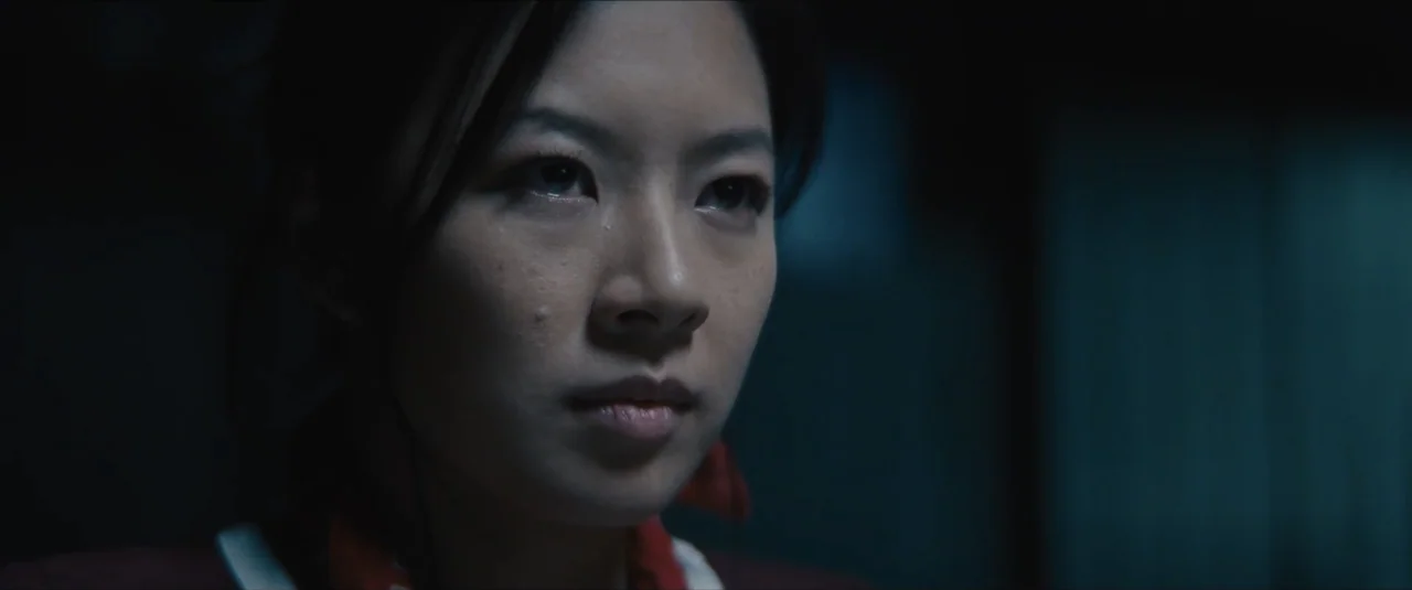 Stalker (2020) movie still: closeup — A dark room serves as the setting for the close-up shot. A woman with dark hair stares directly ahead.