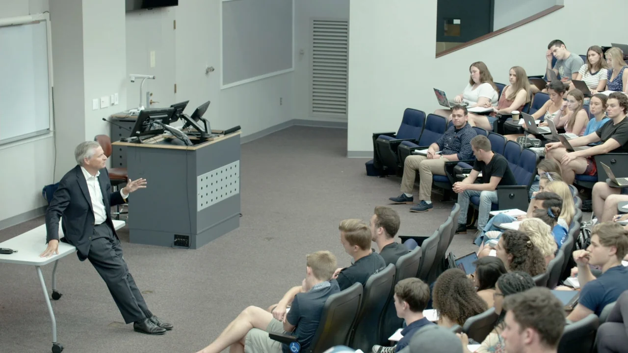 The Soul of America (2020) movie still: wide — A modern university lecture hall contains tiered seating and a front teaching podium. An older man in…