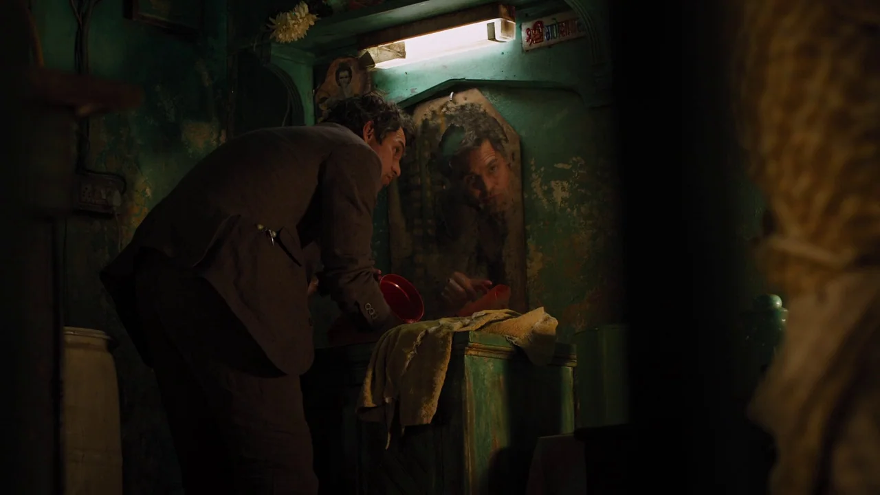 The Avengers (2012) movie still: medium — A dimly lit washroom features peeling teal walls and a weathered mirror above a basin. A man in a dark…