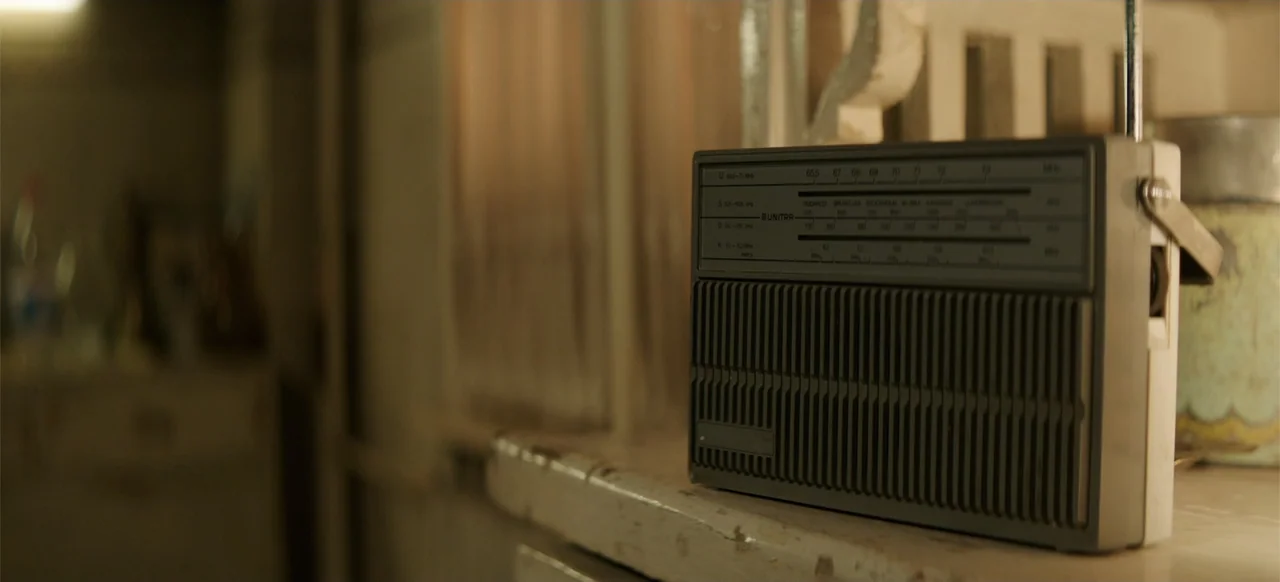 Morir un Poco (1967) movie still: closeup — A vintage Unitra radio sits on a worn wooden shelf in an interior room. The background is blurred and…