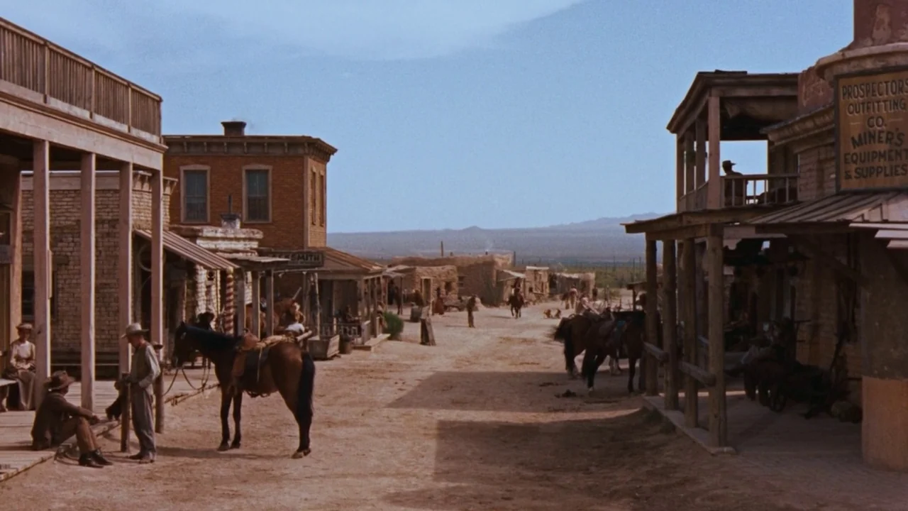 Rio Bravo (1959) movie still: wide — A dusty dirt street runs through a collection of weathered wooden western buildings. Several people stand near…