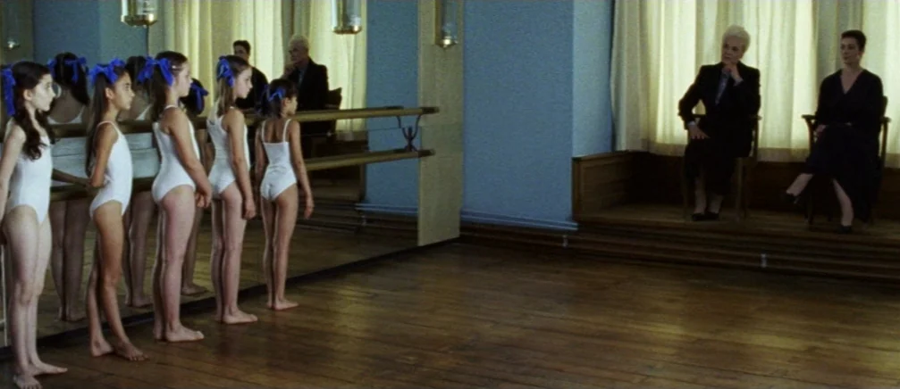 Innocence (2005) movie still: wide — A spacious dance studio with a wood floor, large mirror, and full-length windows. Five young girls in white…