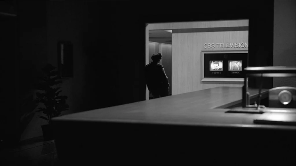 Good Night And Good Luck (2005) movie still: wide — A dark, modern office space leads into a brightly lit television network corridor. A man in…
