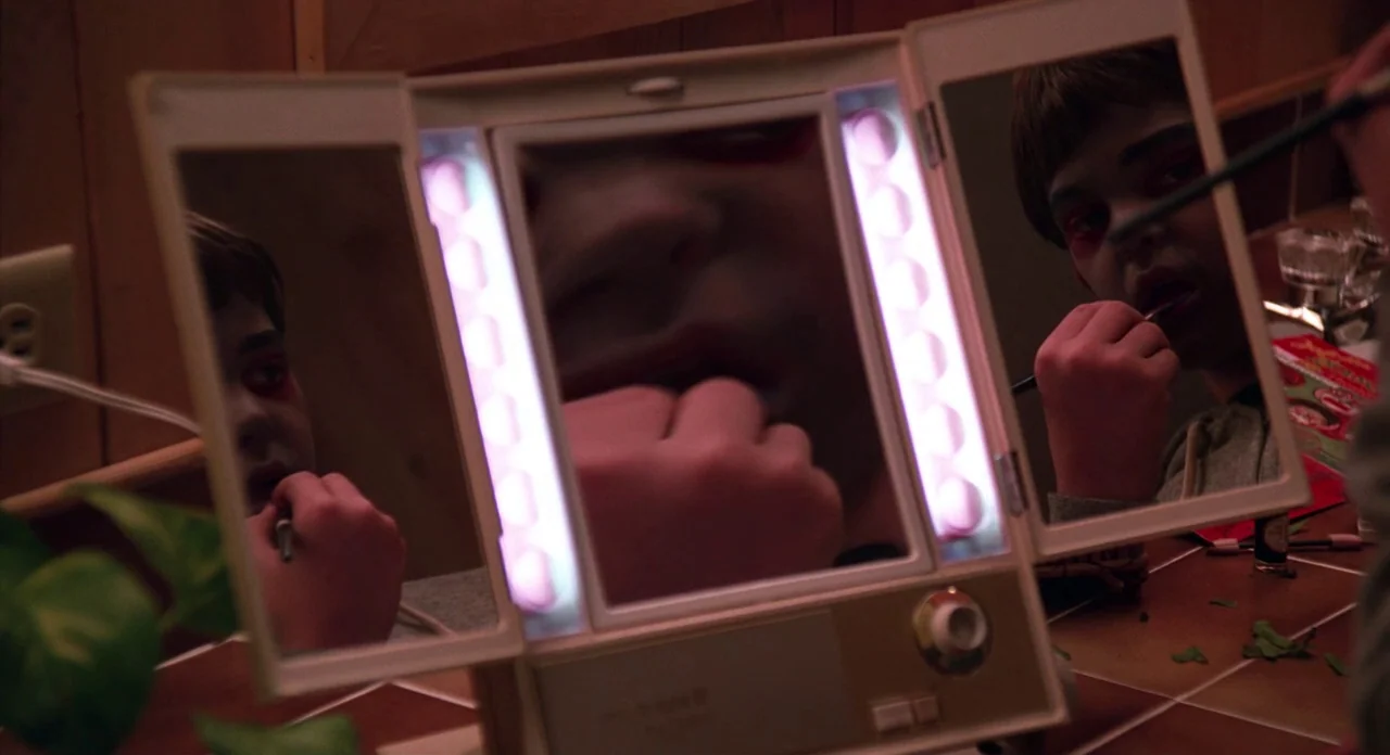 E.T. The Extra-Terrestrial (1982) movie still: closeup — A person sits in front of a tri-fold makeup mirror with integrated side lights. They use a…