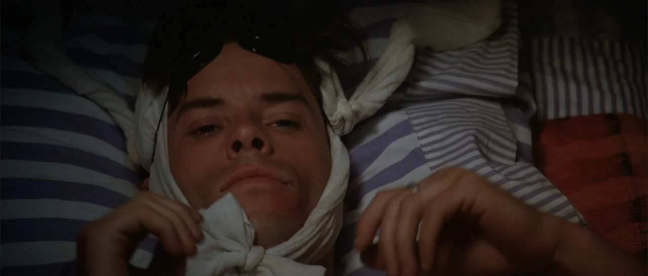 The Adventures of Priscilla, Queen of the Desert (1994) movie still: closeup — A dark bedroom with striped blue and white bedding in soft shadows. A…