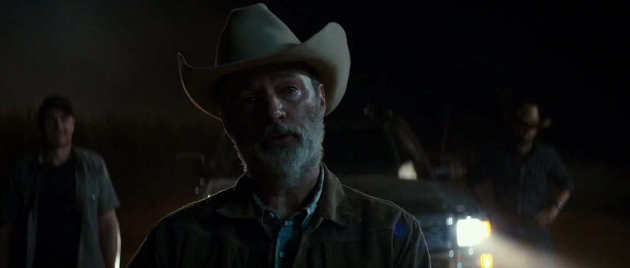Logan (2017) movie still: medium — A dark rural field at night featuring three men near a parked vehicle. The central figure wearing a cowboy hat…
