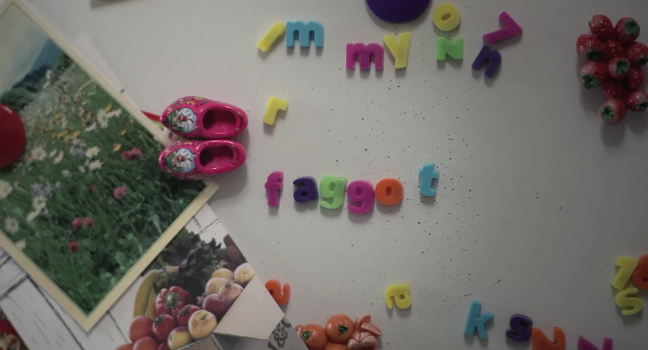 Weekend (2011) movie still: closeup — A white magnetic refrigerator door features arranged colorful plastic letter magnets and small trinkets. Two…