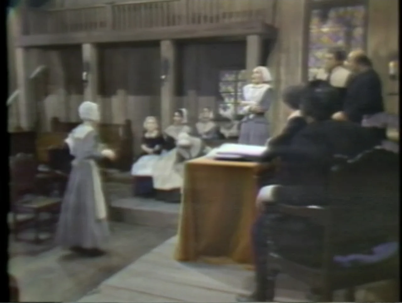 The Crucible (1996) movie still: fullbody — A wooden interior space features benches and a table typical of colonial settings. A group of…