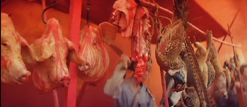Green Snake (1993) movie still: medium — A meat market display features multiple severed pig heads and a pheasant hanging from hooks. The animals…