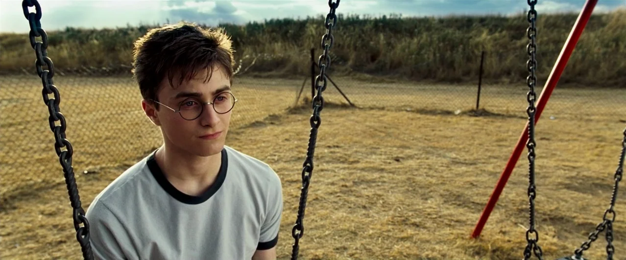 Harry Potter & The Order of the Phoenix (2007) movie still: medium — A dry, grassy, fenced area serves as an outdoor playground. A teenage boy with…