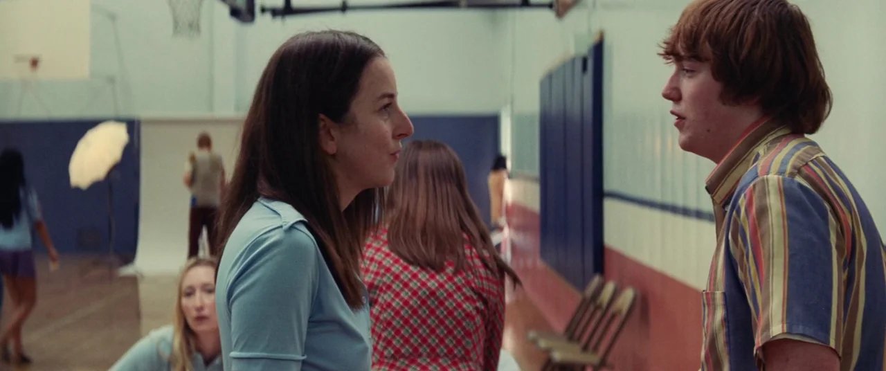 Licorice Pizza (2021) movie still: medium — A high school gymnasium interior with wood flooring and blue and red wall padding. A woman and a young…
