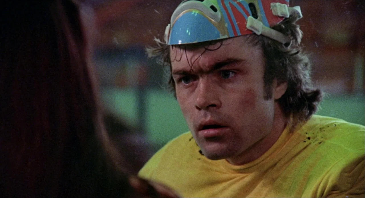 Black Christmas (1974) movie still: closeup — A dimly lit indoor recreational space with visible film texture and muted colors. A man wearing a…
