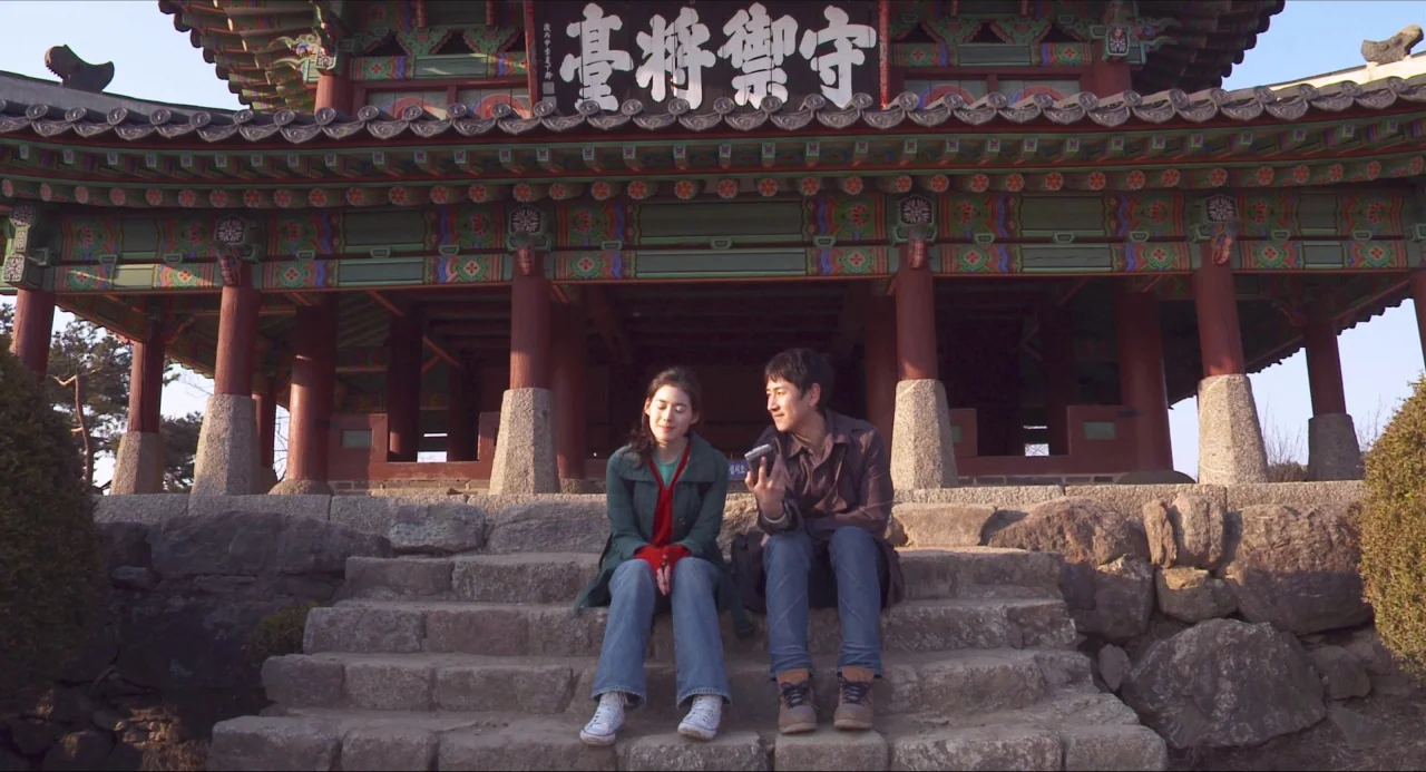 Nobody’s Daughter Haewon (2013) movie still: fullbody — A traditional Korean wooden pavilion sits atop a weathered stone platform. A young man and…
