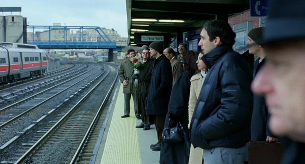 Eternal Sunshine of the Spotless Mind (2004) movie still: wide — A group of people wait on a commuter train platform beneath a covered overhang. A…