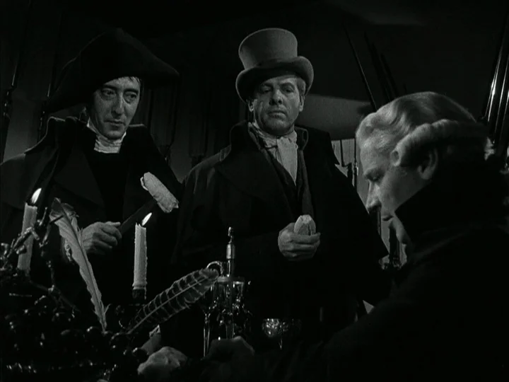 The Black Book (Reign of Terror) (1949) movie still: medium — A dimly lit 19th-century room features three men gathered closely around a candlelit…