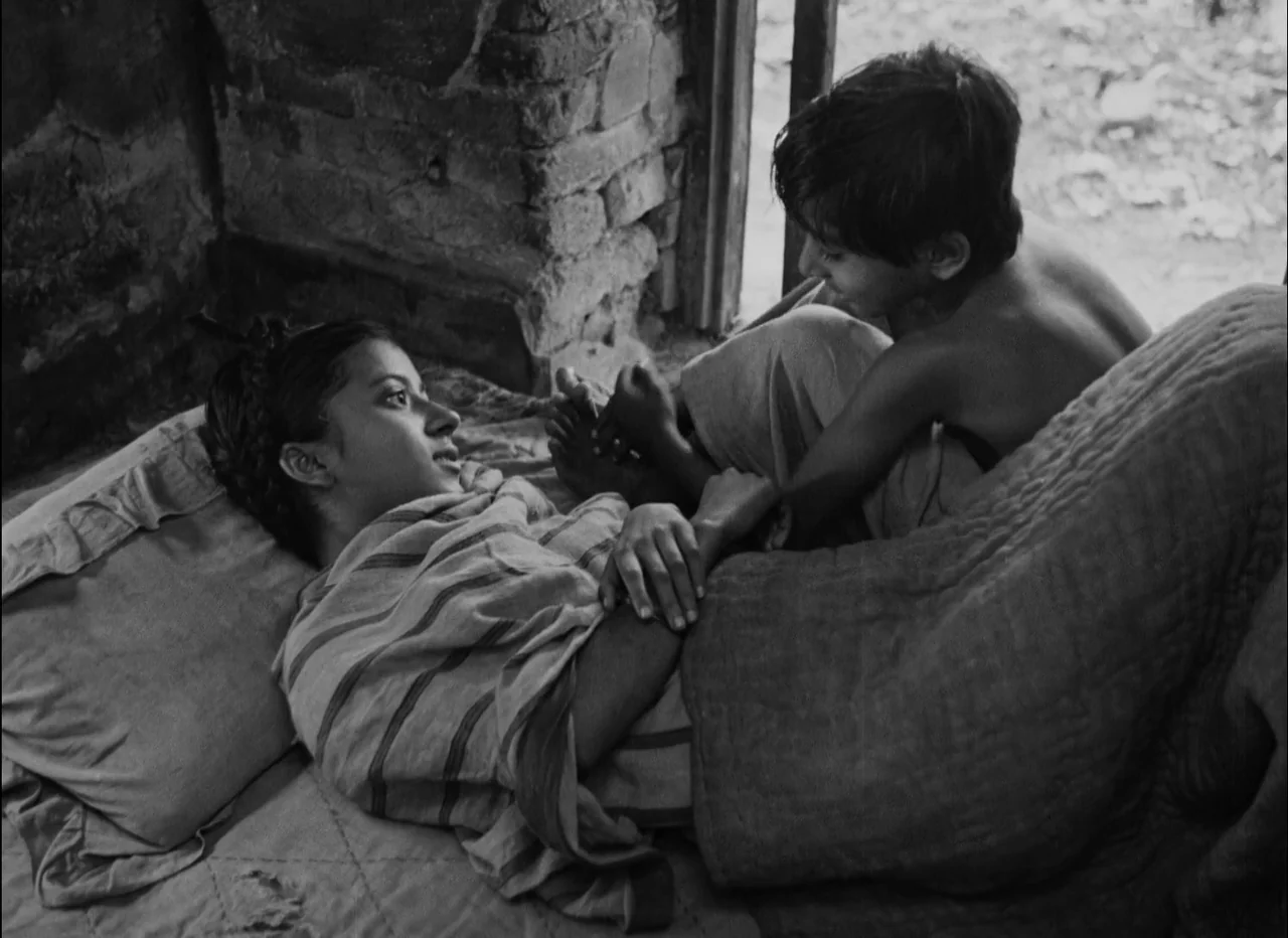 Pather Panchali (1955) movie still: medium — A rustic, sparsely furnished interior with bare brick walls and a simple sleeping mat. A young woman…