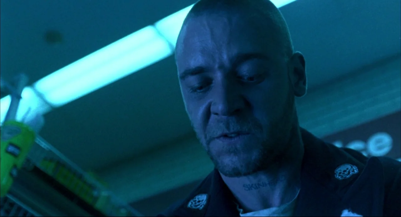 Romper Stomper (1992) movie still: closeup — A dimly lit convenience store at night with harsh blue fluorescent illumination overhead. A man with a…