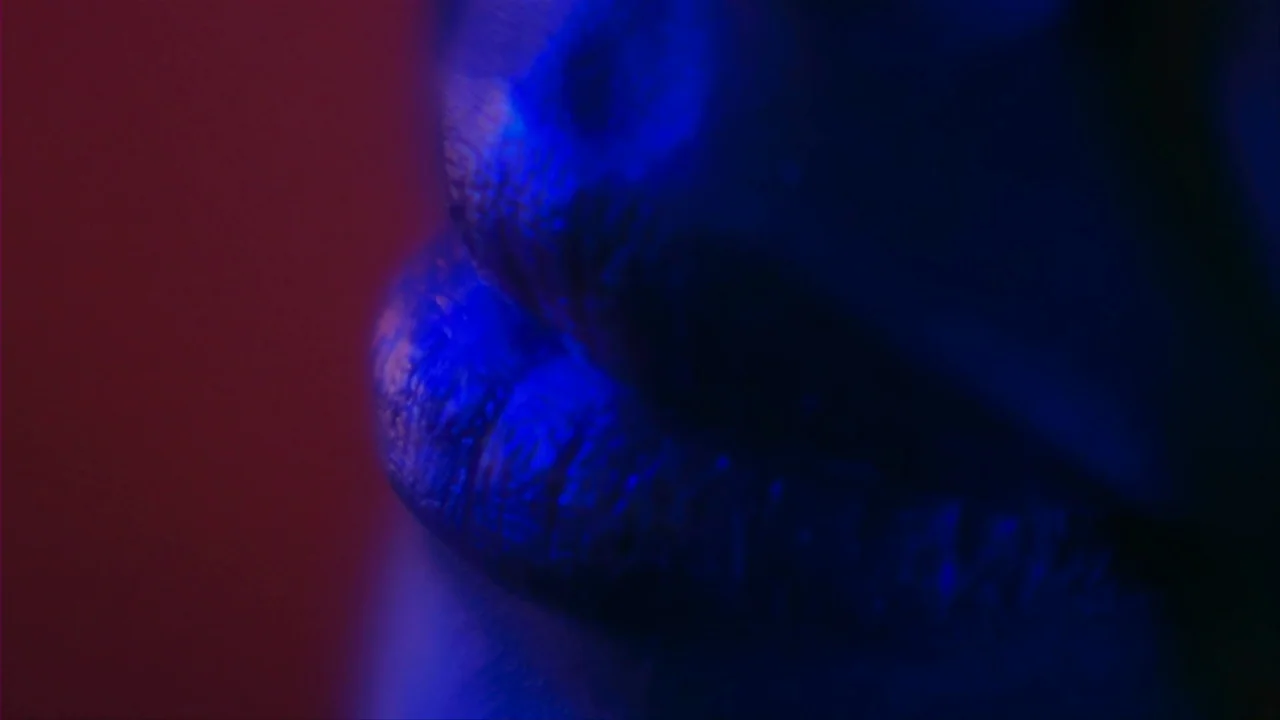 Merantau (2009) movie still: closeup — An extreme close-up of a human mouth against a dark, featureless background. The lips are illuminated by…