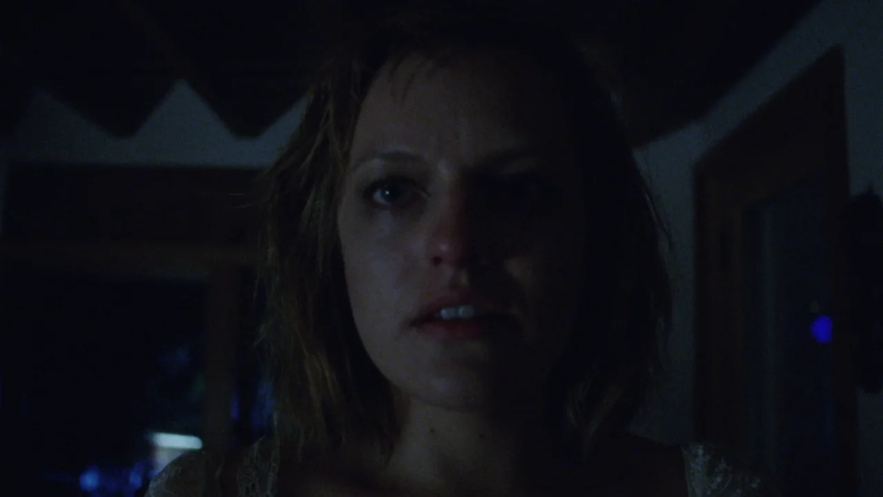 Queen of Earth (2015) movie still: closeup — A dimly lit interior room at night provides an dark and obscured background. A woman looks forward with…