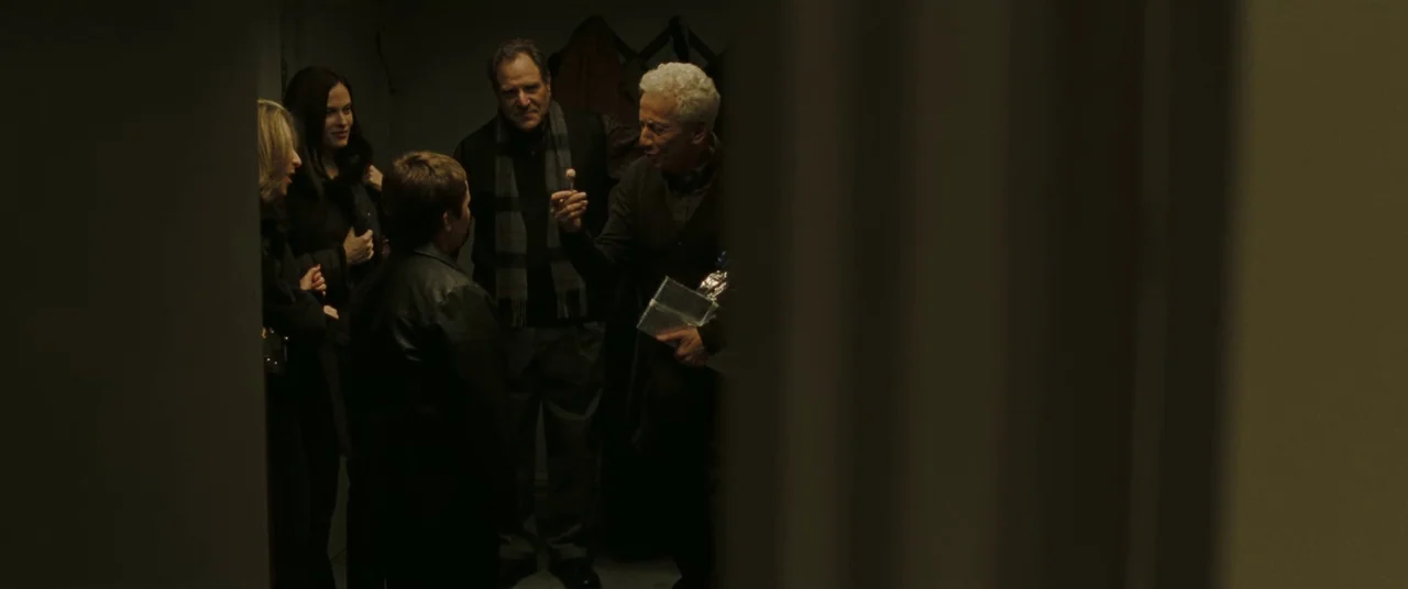 Two Lovers (2008) movie still: medium — A dimly lit interior hallway with a group of people gathered in the background. The man in the foreground…