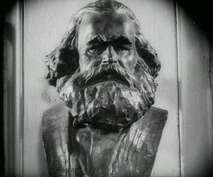 Man with a Movie Camera (1929) movie still: closeup — A stone or bronze bust of Karl Marx stands centered against a paneled wall. The sculpted head…