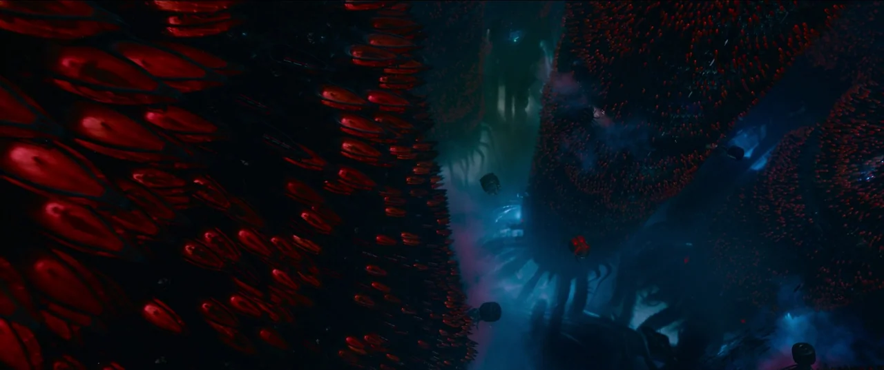 The Matrix Resurrections (2021) movie still: wide — A dark, alien environment contains massive organic pillars covered in shiny, blood-red, pod-like…