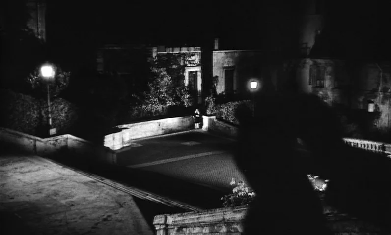 The Girl Who Knew Too Much (1963) movie still: wide — A night view of an empty stone-paved plaza illuminated by two tall streetlamps. The scene…