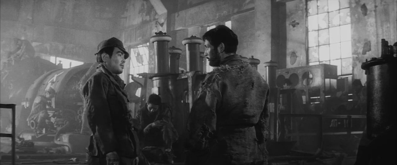 The Human Condition III: A Soldier’s Prayer (1961) movie still: medium — A dilapidated industrial interior with large machines and high windows…