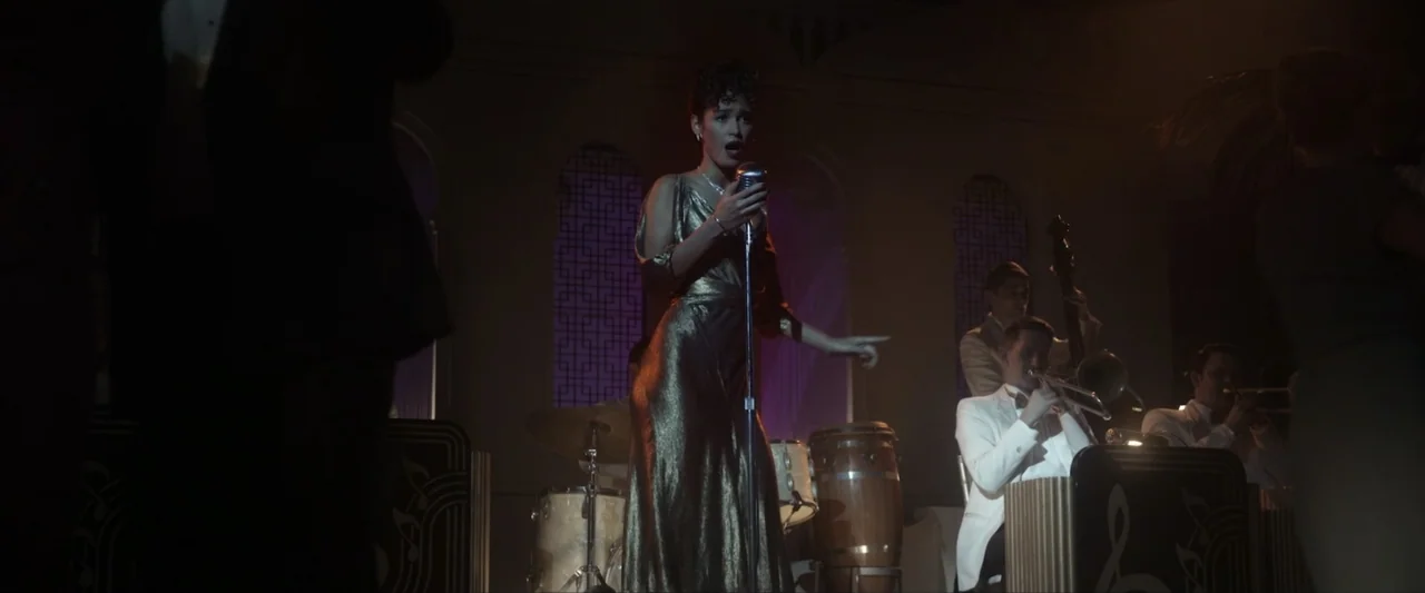 Reagan (2024) movie still: medium — A jazz band performs on a dimly lit club stage with decorative arched backdrop panels. A female singer in a gold…