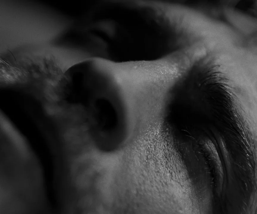 The Lighthouse (2019) movie still: closeup — A close-up view of a man's face in high contrast black and white. The man has his eyes closed while…