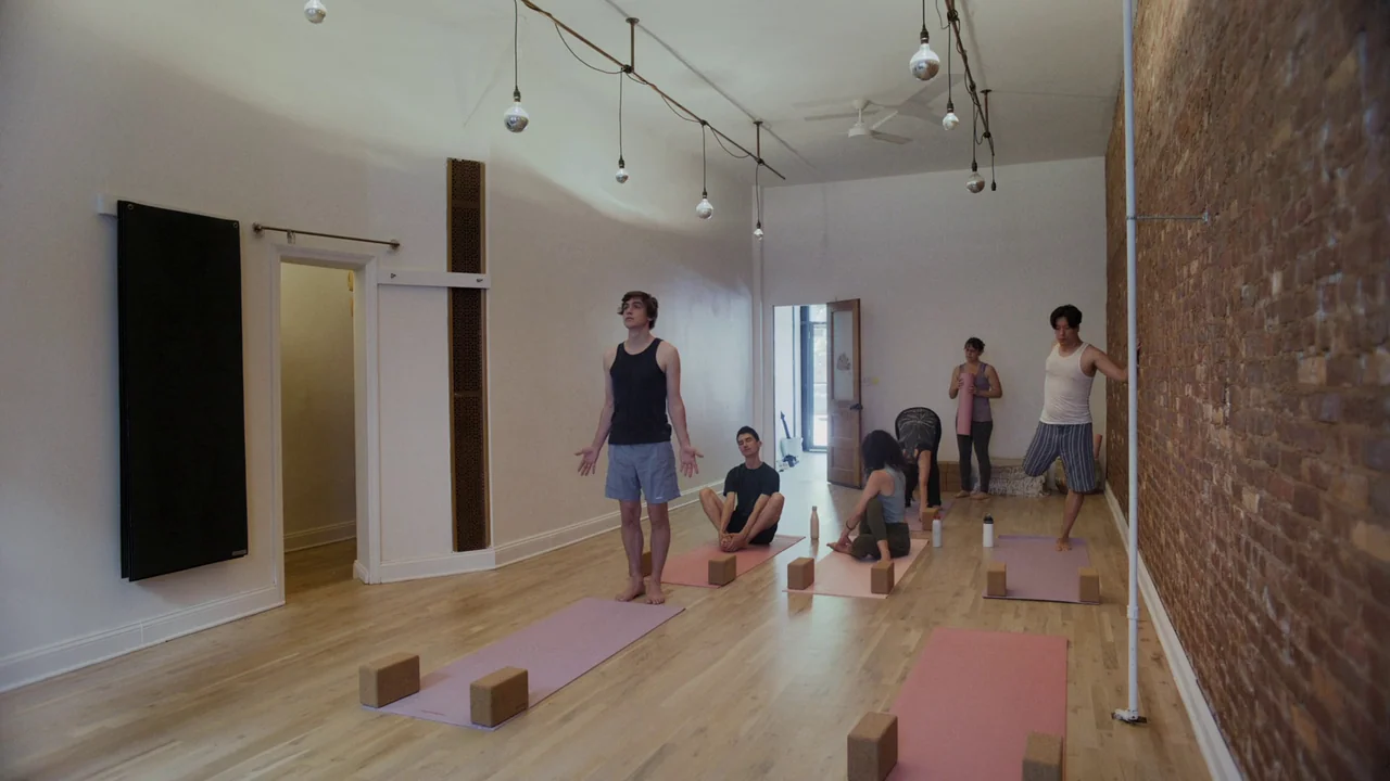 The Feeling That the Time for Doing Something Has Passed (2023) movie still: wide — A spacious room with exposed brick walls and hardwood floors…