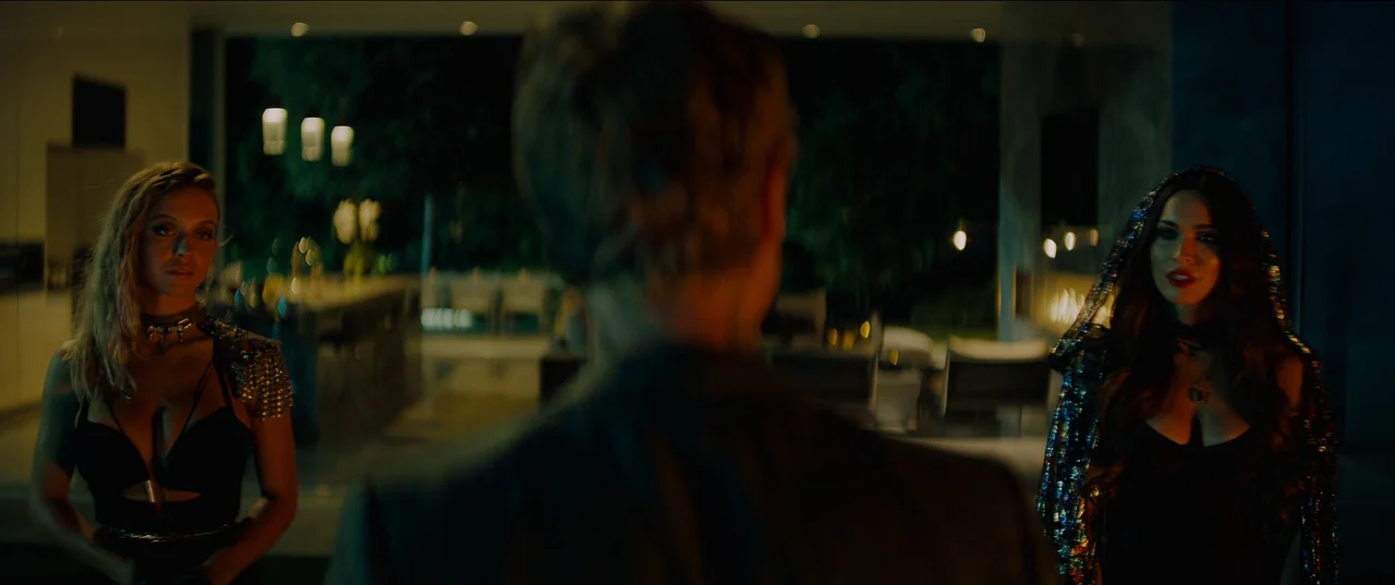 Night Teeth (2021) movie still: medium — A dark modern interior with glass walls looking out onto a nighttime garden patio. A man faces two women…