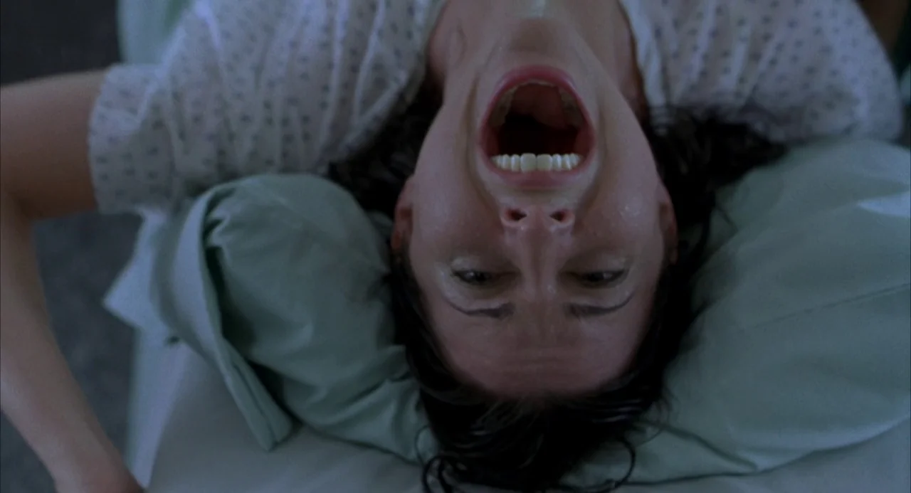 Hulk (2003) movie still: closeup — A hospital patient lies on a bed, her head positioned toward the camera. She looks upward with her mouth wide…