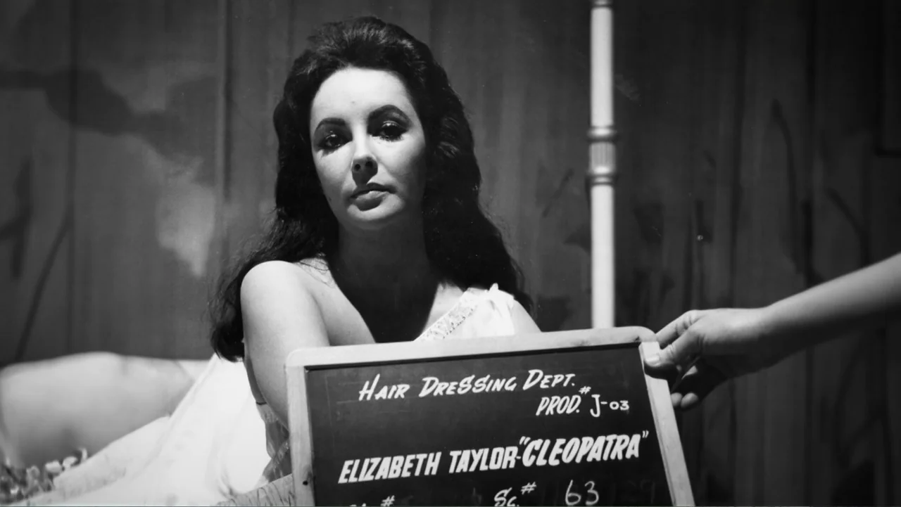 Elizabeth Taylor: The Lost Tapes (2024) movie still: medium — A film set hairdressing station features a blank wall background with a light stand…