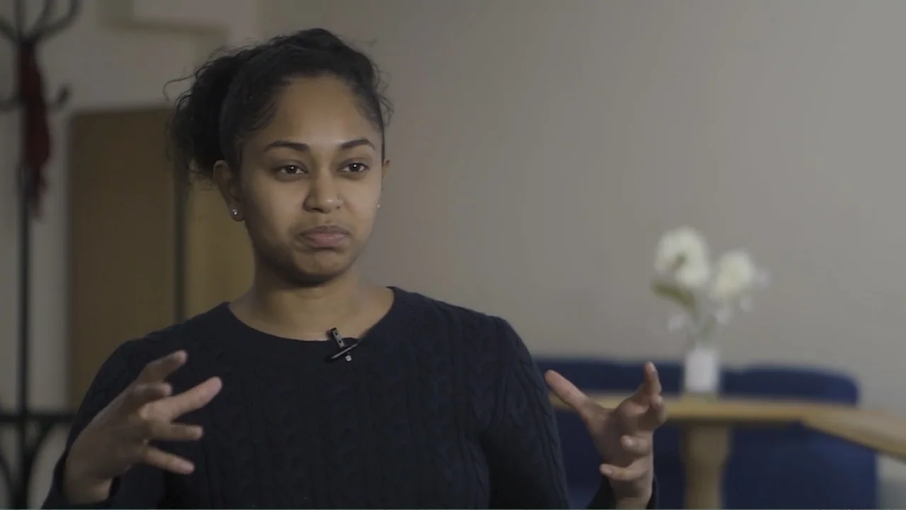 A Film Called Blacks Can't Swim (My Journey My Story) (2020) movie still: medium — A person sits in a softly lit room with neutral colored walls.…